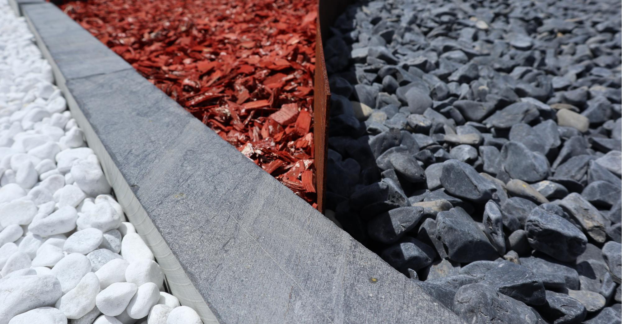 Galets blancs de Carrare, bordure Ardesia en ardoise, copeaux de bois rouges, galets noirs Igea